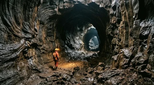 Explorateur équipé de matériel de spéléologie progressant dans un tunnel de lave volcanique aux reflets brillants