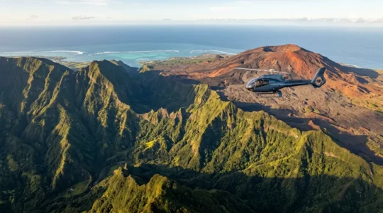 Vue aérienne d'un hélicoptère survolant les cirques verdoyants et le volcan de la Réunion avec le lagon en arrière-plan