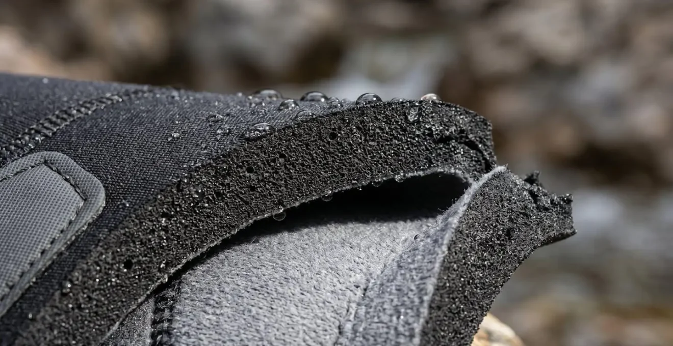 Gros plan macro sur la texture épaisse du néoprène avec des gouttes d'eau perlant sur la surface et des renforts visibles aux articulations