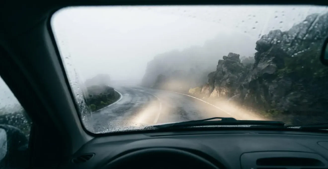 Route de montagne disparaissant dans une épaisse mer de nuages avec véhicule aux phares allumés